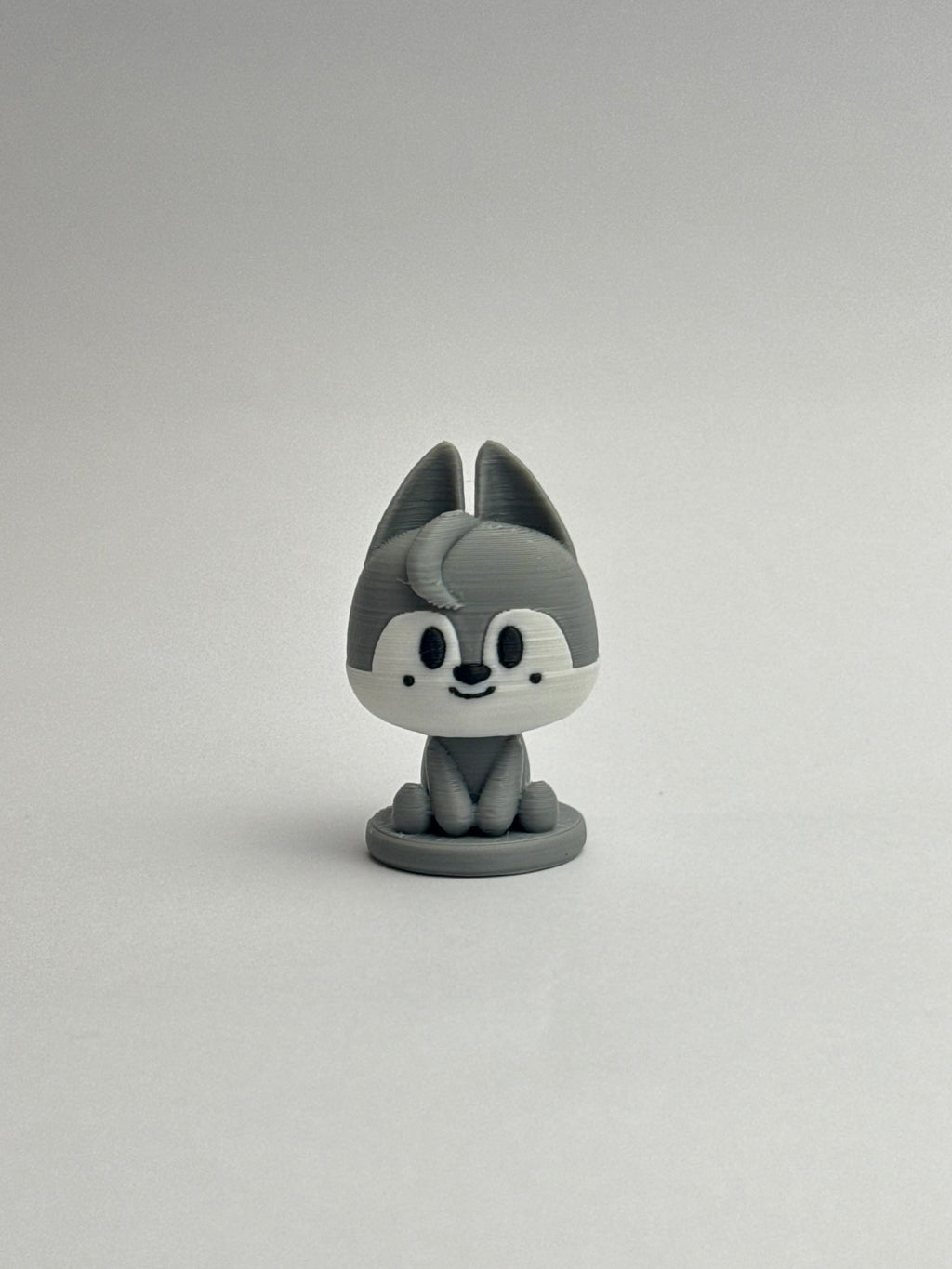 Gray cartoon-like figurine with a white face on a plain background